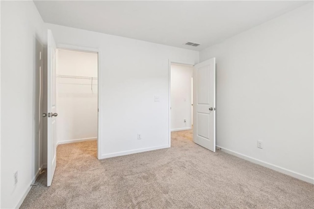 unfurnished bedroom with a walk in closet, a closet, and light colored carpet