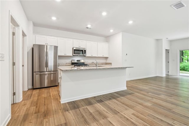 kitchen with stainless steel appliances, white cabinetry, light hardwood / wood-style floors, and an island with sink