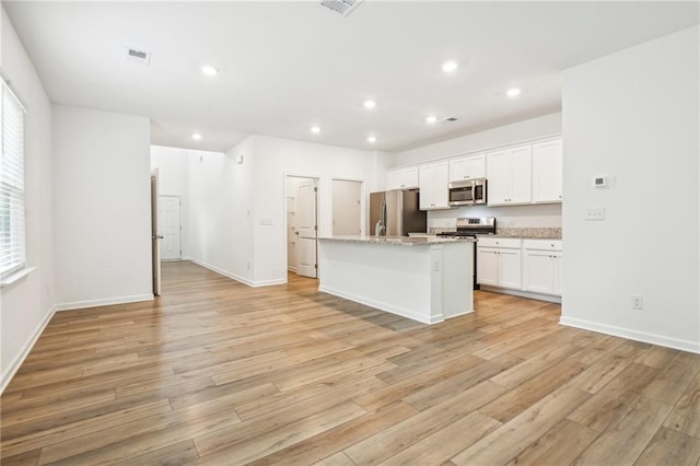 kitchen with white cabinets, light wood-type flooring, stainless steel appliances, and an island with sink