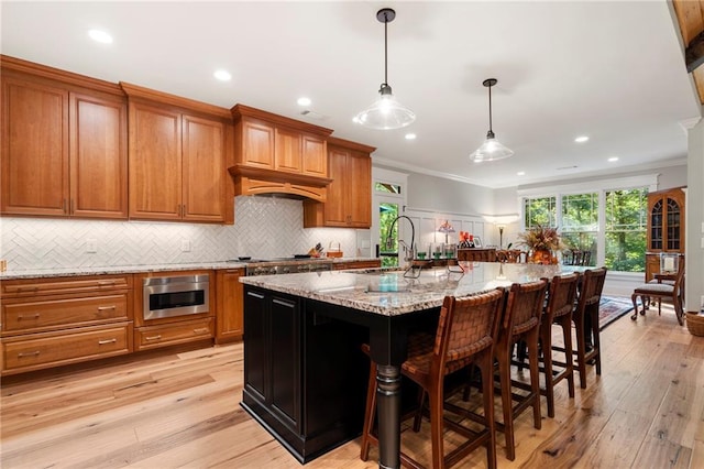 kitchen with an island with sink, hanging light fixtures, ornamental molding, and light hardwood / wood-style flooring