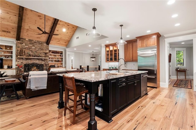 kitchen with light stone counters, vaulted ceiling with beams, a kitchen island with sink, a fireplace, and light wood-type flooring