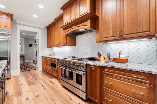 kitchen with light stone counters, light hardwood / wood-style flooring, high quality appliances, crown molding, and decorative backsplash