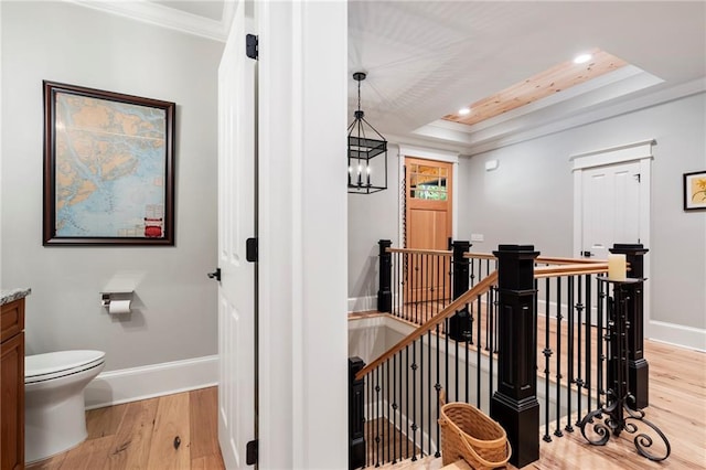 hall featuring ornamental molding, light wood-type flooring, a tray ceiling, and a chandelier