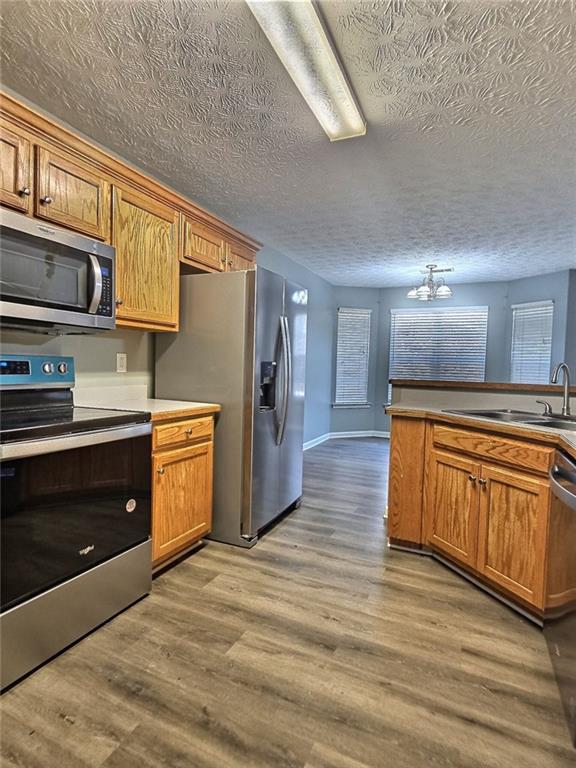 kitchen featuring sink, appliances with stainless steel finishes, wood-type flooring, a textured ceiling, and a chandelier