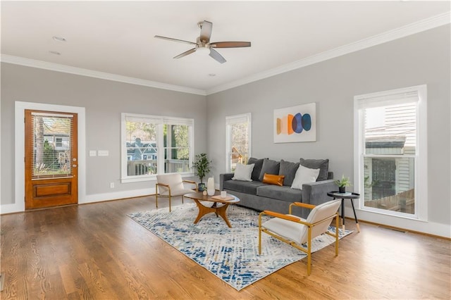 living area featuring baseboards, wood finished floors, ornamental molding, and a ceiling fan