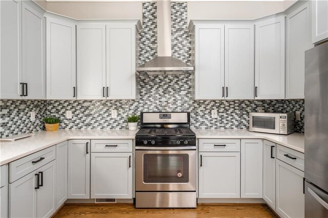 kitchen featuring decorative backsplash, light countertops, wall chimney exhaust hood, and appliances with stainless steel finishes