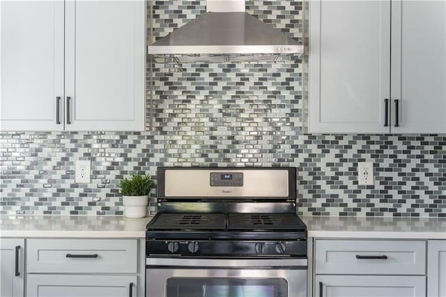 kitchen featuring wall chimney range hood, light countertops, stainless steel gas range oven, and backsplash