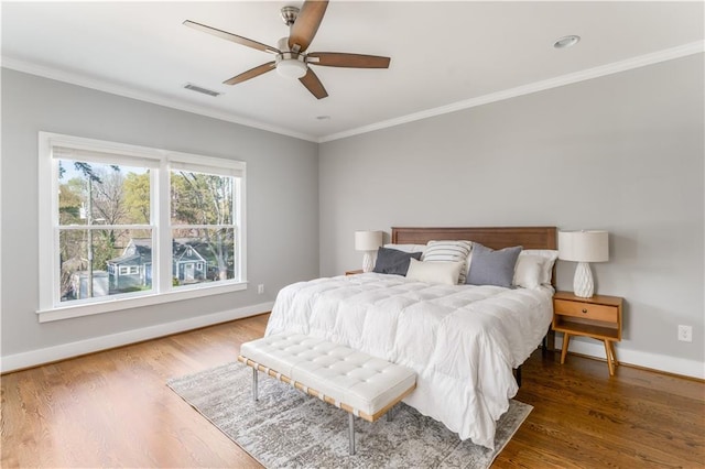 bedroom with baseboards, visible vents, crown molding, and wood finished floors