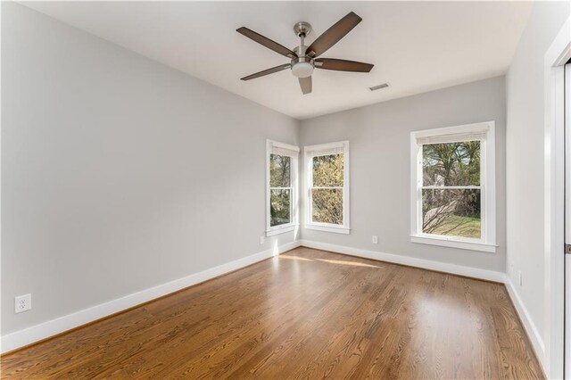 spare room with wood finished floors, a wealth of natural light, baseboards, and visible vents