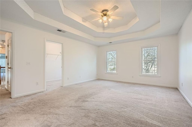 carpeted empty room with a raised ceiling and ceiling fan