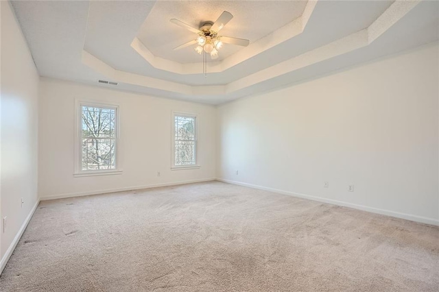 carpeted empty room with a raised ceiling and ceiling fan