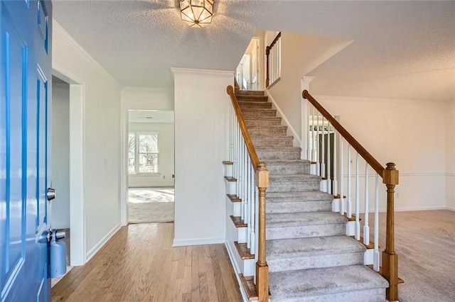 stairway featuring crown molding, wood-type flooring, and a textured ceiling