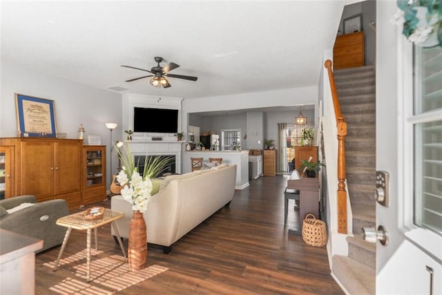 living area with a ceiling fan, a textured ceiling, dark wood finished floors, stairway, and a fireplace