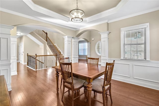 dining space featuring arched walkways, a raised ceiling, decorative columns, and wood finished floors