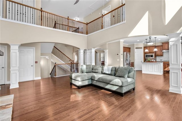 living area with dark wood finished floors, decorative columns, arched walkways, and stairs