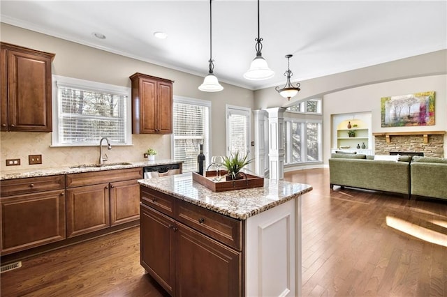 kitchen featuring dark wood-style flooring, a sink, hanging light fixtures, ornamental molding, and decorative columns