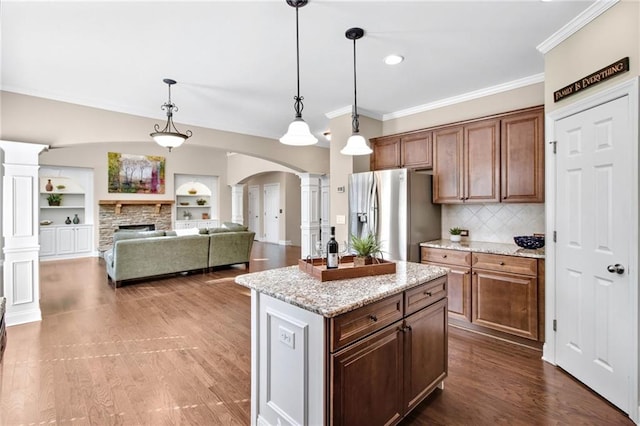 kitchen featuring arched walkways, crown molding, a stone fireplace, stainless steel fridge, and ornate columns