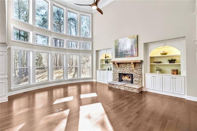 unfurnished living room featuring a stone fireplace, wood finished floors, and built in features