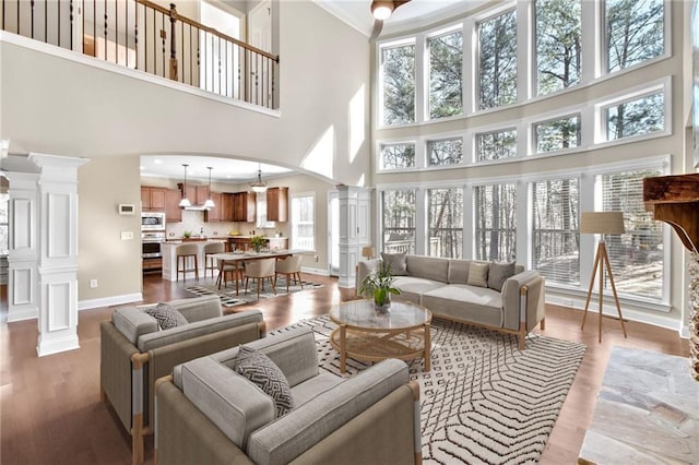 living area with crown molding, light wood-style flooring, decorative columns, and baseboards