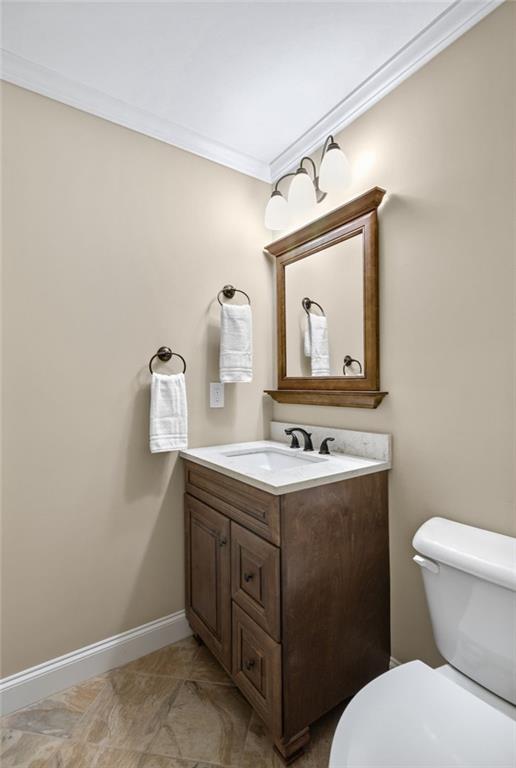 bathroom with toilet, ornamental molding, vanity, and baseboards