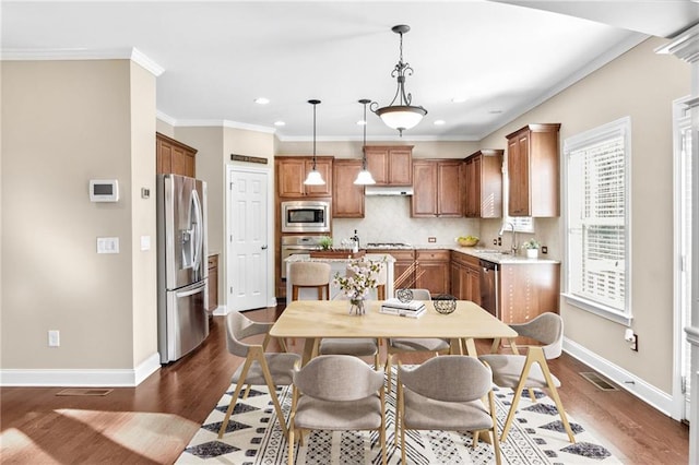 kitchen featuring appliances with stainless steel finishes, brown cabinets, decorative backsplash, and ornamental molding