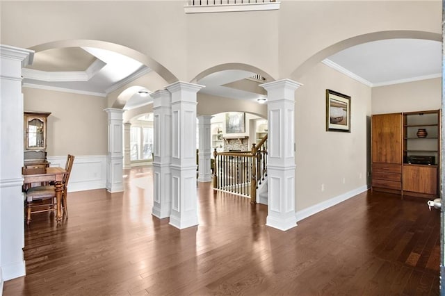 interior space featuring dark wood finished floors, a raised ceiling, stairs, crown molding, and ornate columns