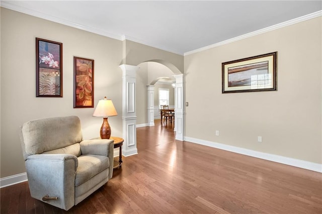 sitting room with ornate columns, arched walkways, wood finished floors, and ornamental molding