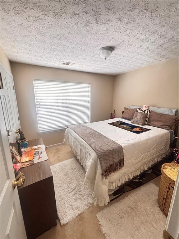 bedroom featuring a textured ceiling, visible vents, and carpet floors