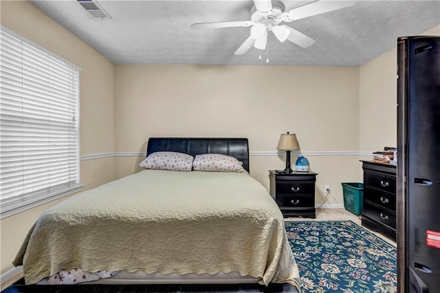 bedroom with a textured ceiling, visible vents, a ceiling fan, and baseboards