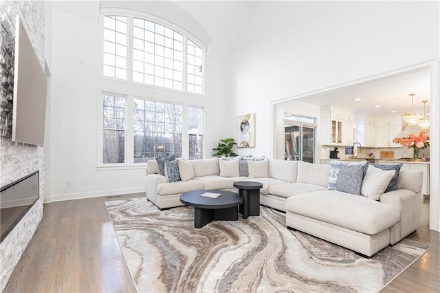 living room featuring sink, a stone fireplace, dark hardwood / wood-style floors, and a high ceiling