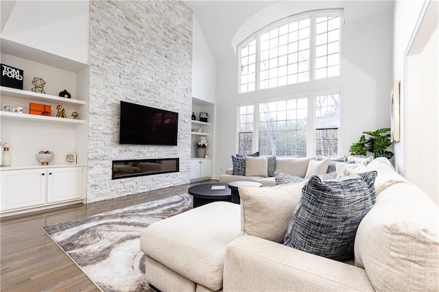 living room with high vaulted ceiling, hardwood / wood-style floors, a fireplace, and built in shelves