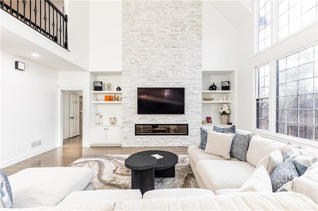 living room featuring a stone fireplace, wood-type flooring, built in features, and a towering ceiling