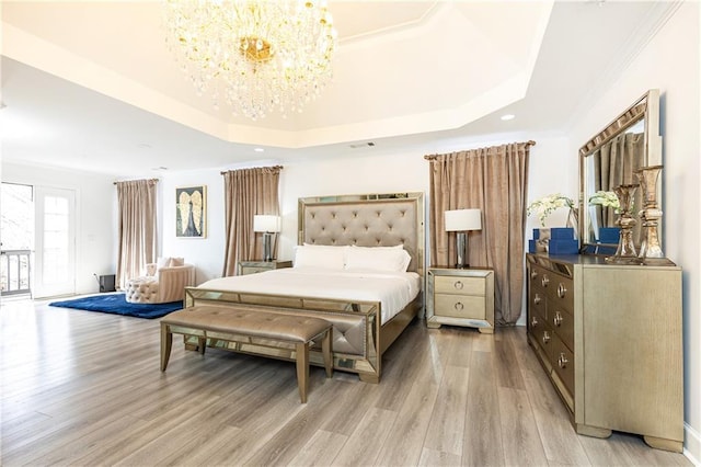 bedroom with light hardwood / wood-style flooring, an inviting chandelier, and a tray ceiling