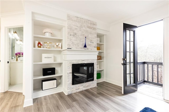 unfurnished living room featuring crown molding, wood-type flooring, a stone fireplace, and built in shelves