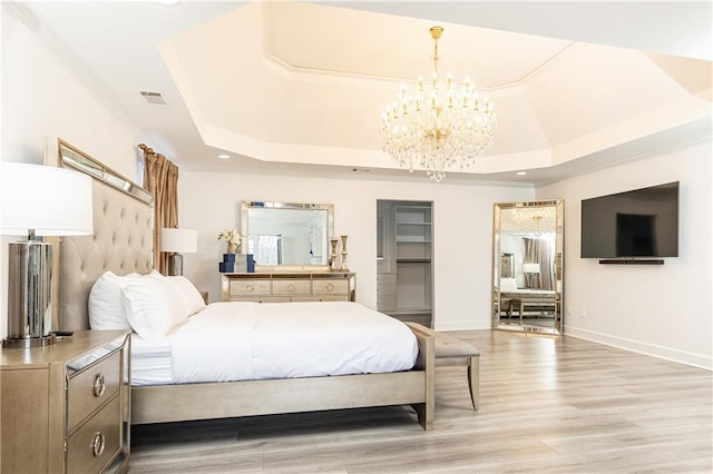 bedroom with a chandelier, a raised ceiling, and light hardwood / wood-style floors