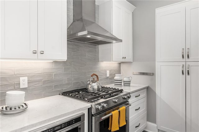 kitchen featuring white cabinetry, backsplash, light stone countertops, wall chimney exhaust hood, and gas range