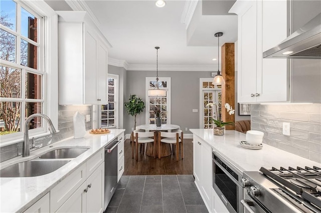 kitchen featuring a sink, white cabinetry, appliances with stainless steel finishes, wall chimney exhaust hood, and crown molding