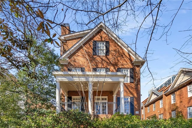 view of front of house with covered porch, a chimney, and brick siding