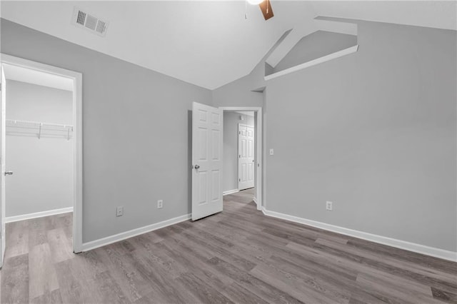 unfurnished bedroom featuring a spacious closet, vaulted ceiling, light hardwood / wood-style flooring, a closet, and ceiling fan