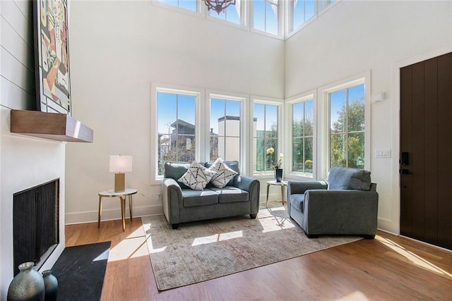 living area with a fireplace, wood finished floors, a towering ceiling, and baseboards