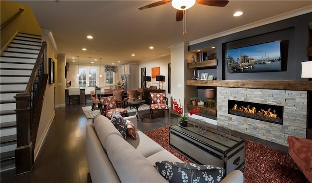 living room with crown molding, a stone fireplace, dark wood-type flooring, and ceiling fan