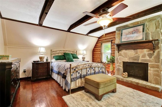 bedroom featuring dark hardwood / wood-style floors, ceiling fan, a fireplace, and vaulted ceiling with beams