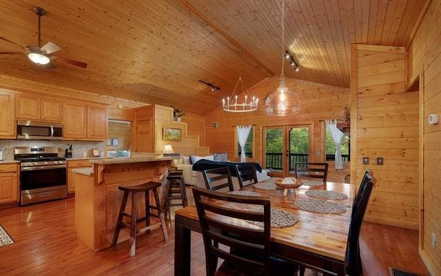 dining room with wooden walls, high vaulted ceiling, wooden ceiling, ceiling fan with notable chandelier, and hardwood / wood-style floors