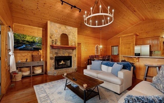 living room with lofted ceiling, an inviting chandelier, wooden walls, a stone fireplace, and wooden ceiling