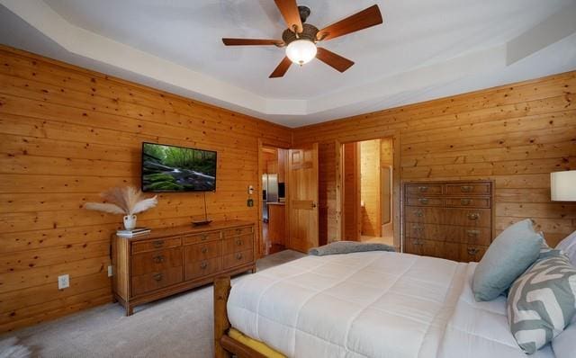 bedroom with a raised ceiling, wood walls, ceiling fan, and light colored carpet