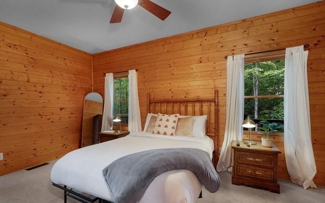 carpeted bedroom featuring multiple windows, wooden walls, and ceiling fan