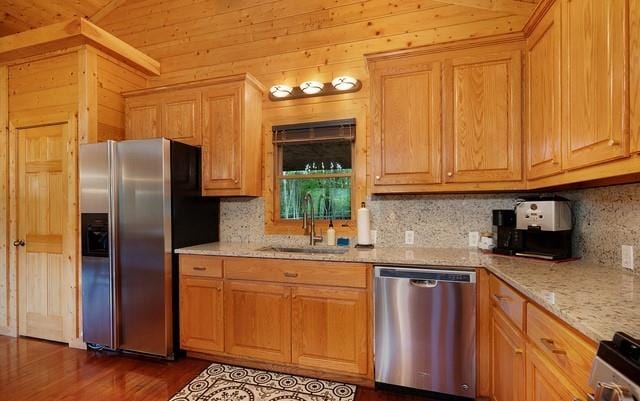 kitchen with light stone counters, sink, wooden walls, appliances with stainless steel finishes, and dark hardwood / wood-style flooring