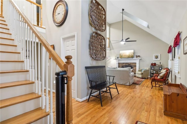 foyer entrance featuring a fireplace, light wood-type flooring, high vaulted ceiling, a skylight, and ceiling fan