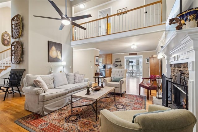 living room with a stone fireplace, a towering ceiling, hardwood / wood-style flooring, ornamental molding, and ceiling fan