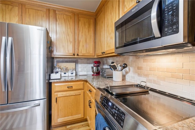 kitchen with appliances with stainless steel finishes, light hardwood / wood-style floors, backsplash, and light stone countertops